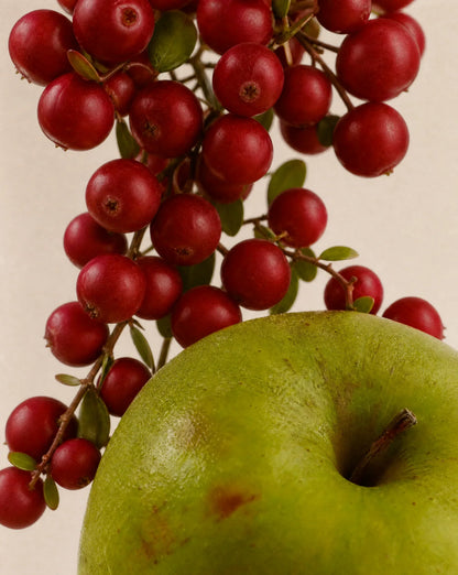Green apple with red berries on a beige background