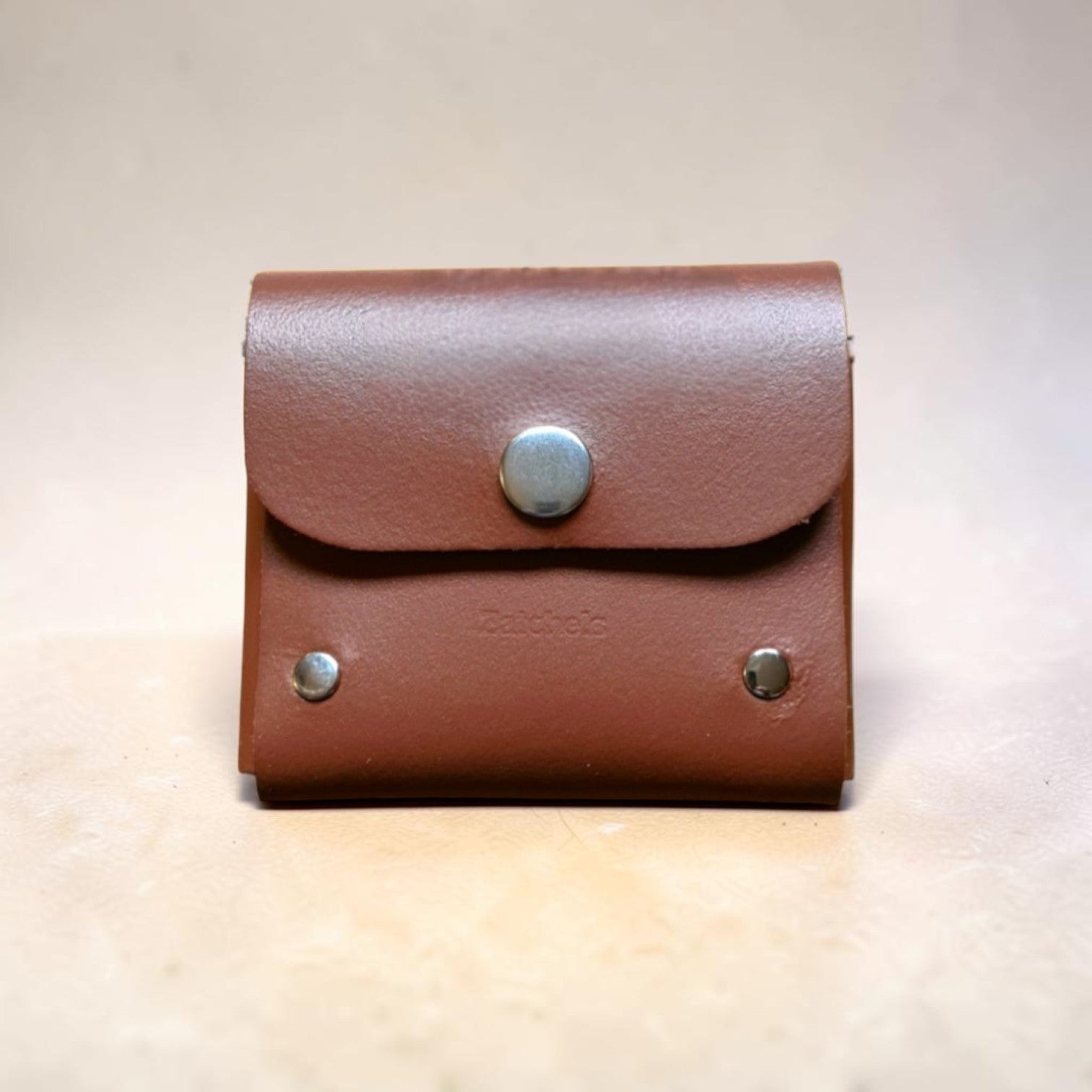 Brown leather pouch with silver buttons on a beige background