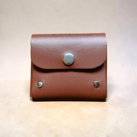 Brown leather pouch with silver buttons on a beige background