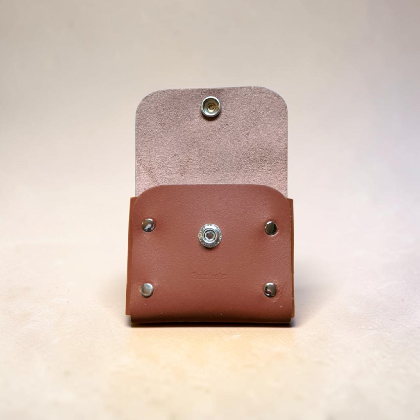 Two leather pouches, one brown and one beige, with metal studs on a light background.