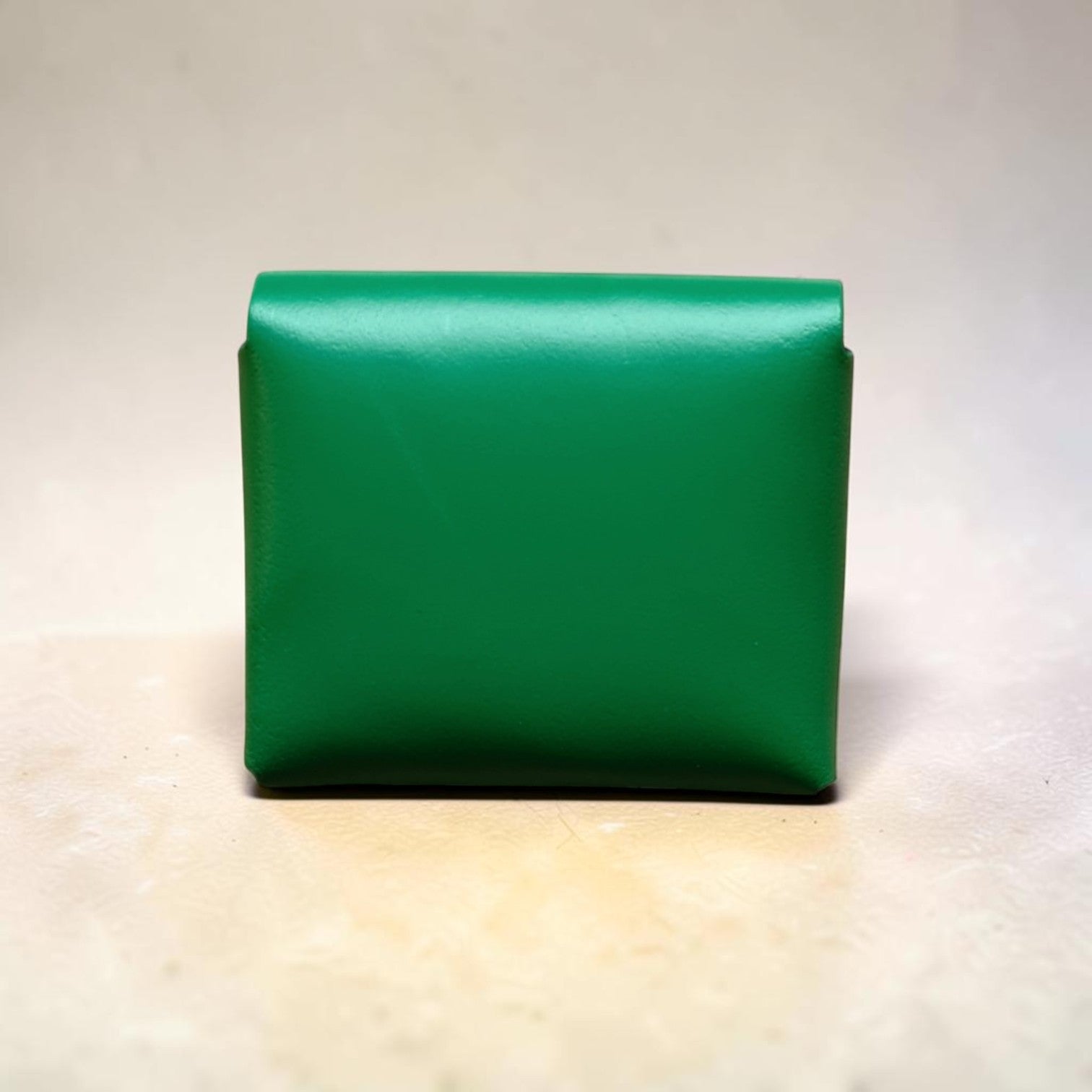 Green leather clutch bag on a light wooden surface