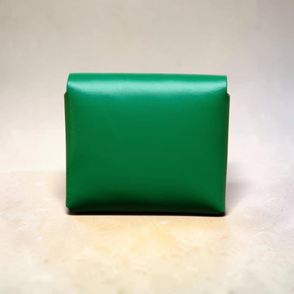 Green leather clutch bag on a light wooden surface