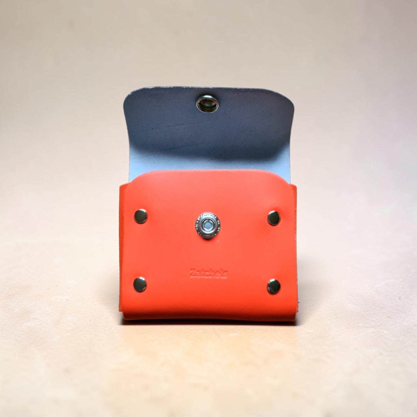 Two leather pouches, one blue and one red, with metal grommets on a light background.