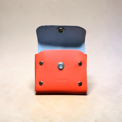 Two leather pouches, one blue and one red, with metal grommets on a light background.
