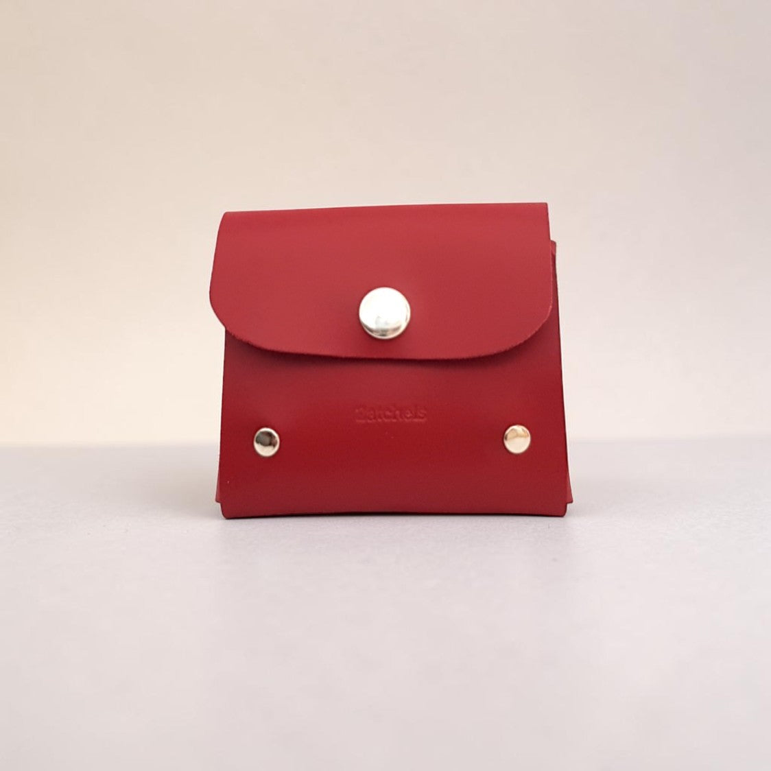 Red leather pouch with silver buttons on a light beige background