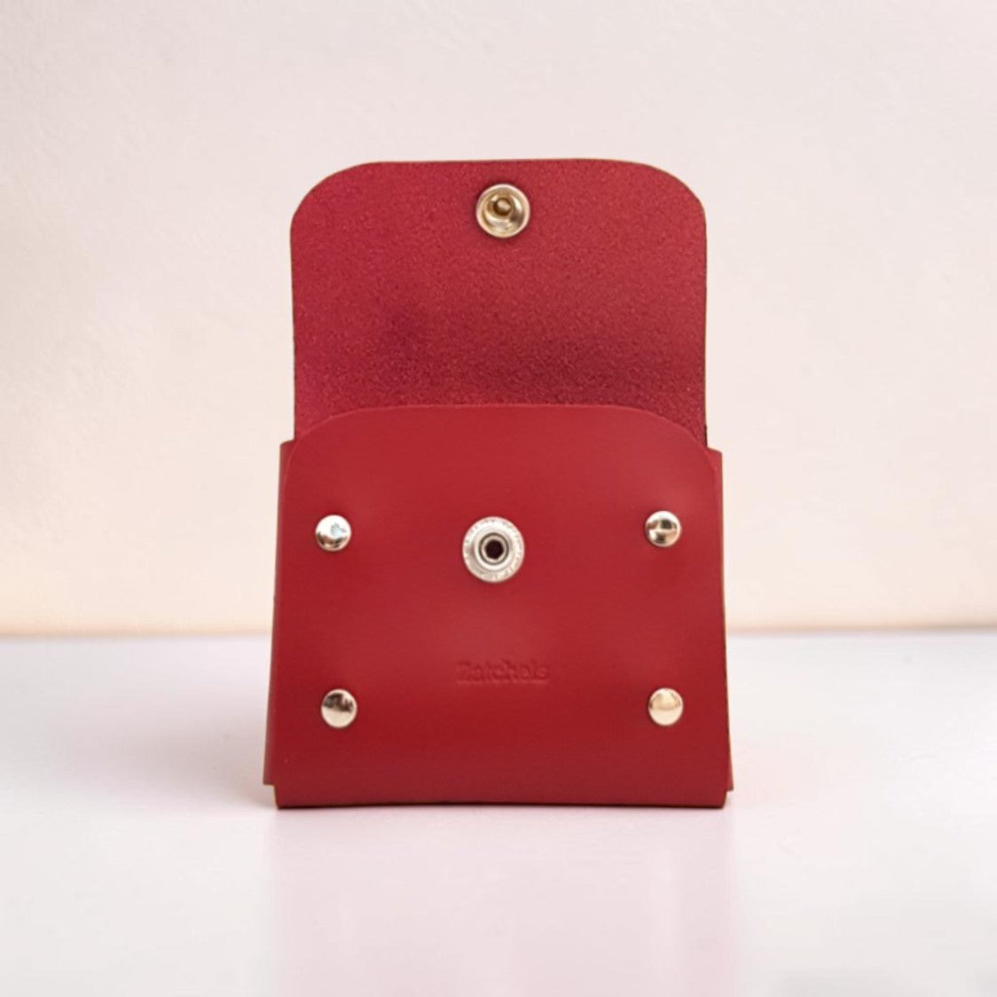 Red leather wallet with gold and silver accents on a light pink background