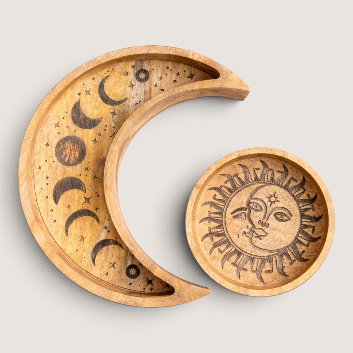 Crescent moon tray with carved moon phases and stars beside a round tray carved with a sun and crescent moon face
