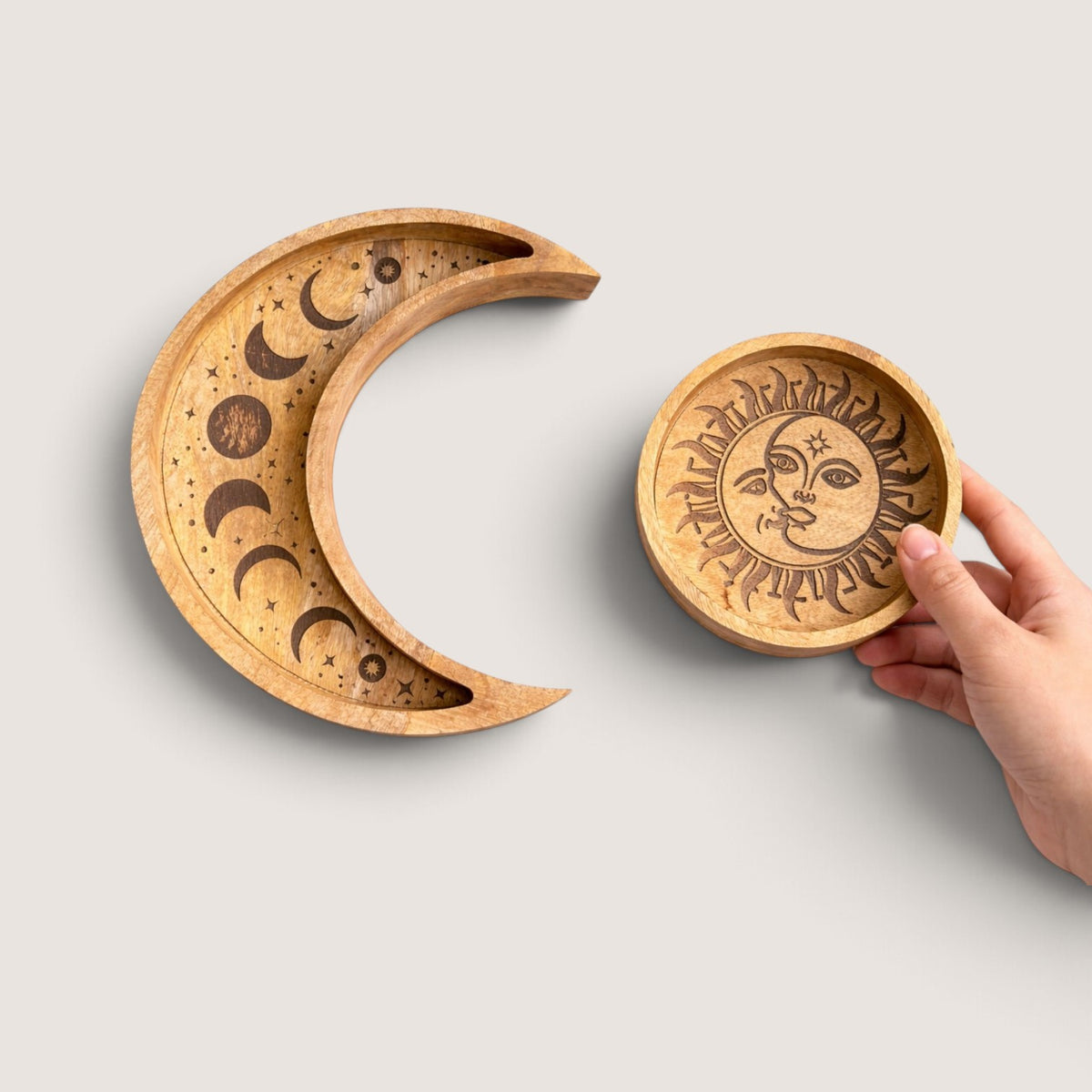 Hand holding the round sun tray beside the crescent moon tray, showing the size of the Sun and Moon wooden tray set