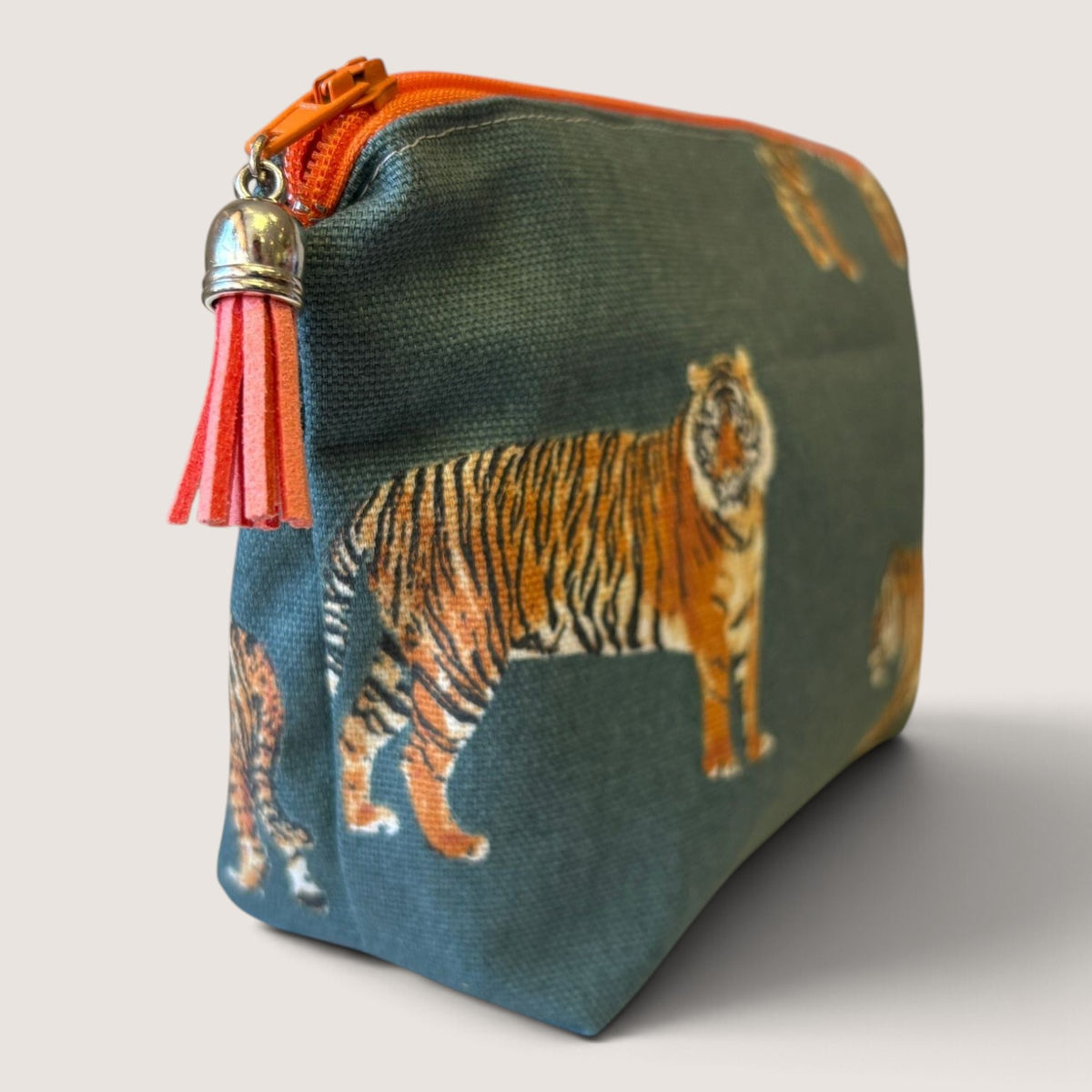 Tiger Tiger everyday pouch in a tiger print on deep teal, with an orange zip and coral suede tassel, angled view
