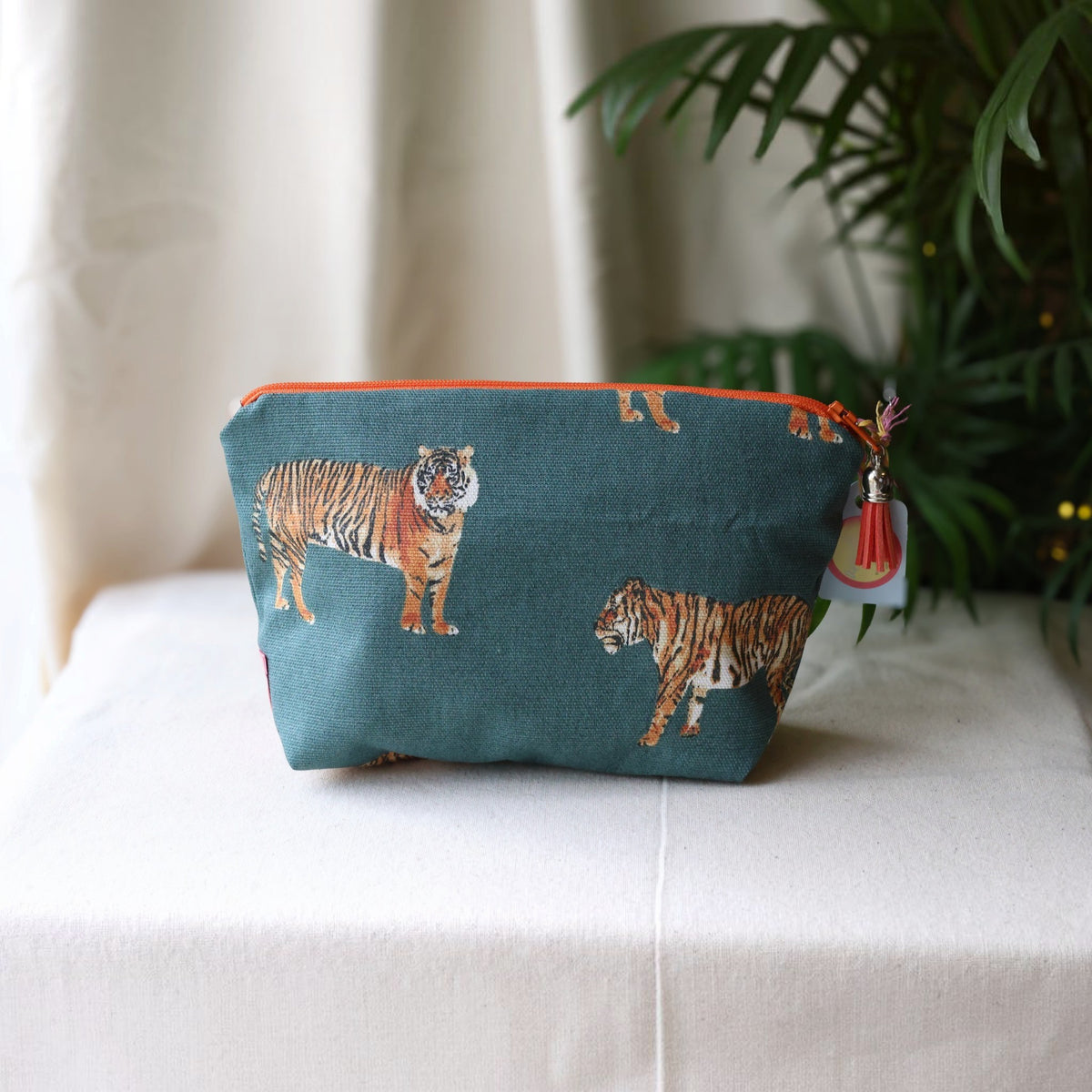 Tiger Tiger everyday pouch with an orange zip and orange tassel on a cream cloth beside a palm plant