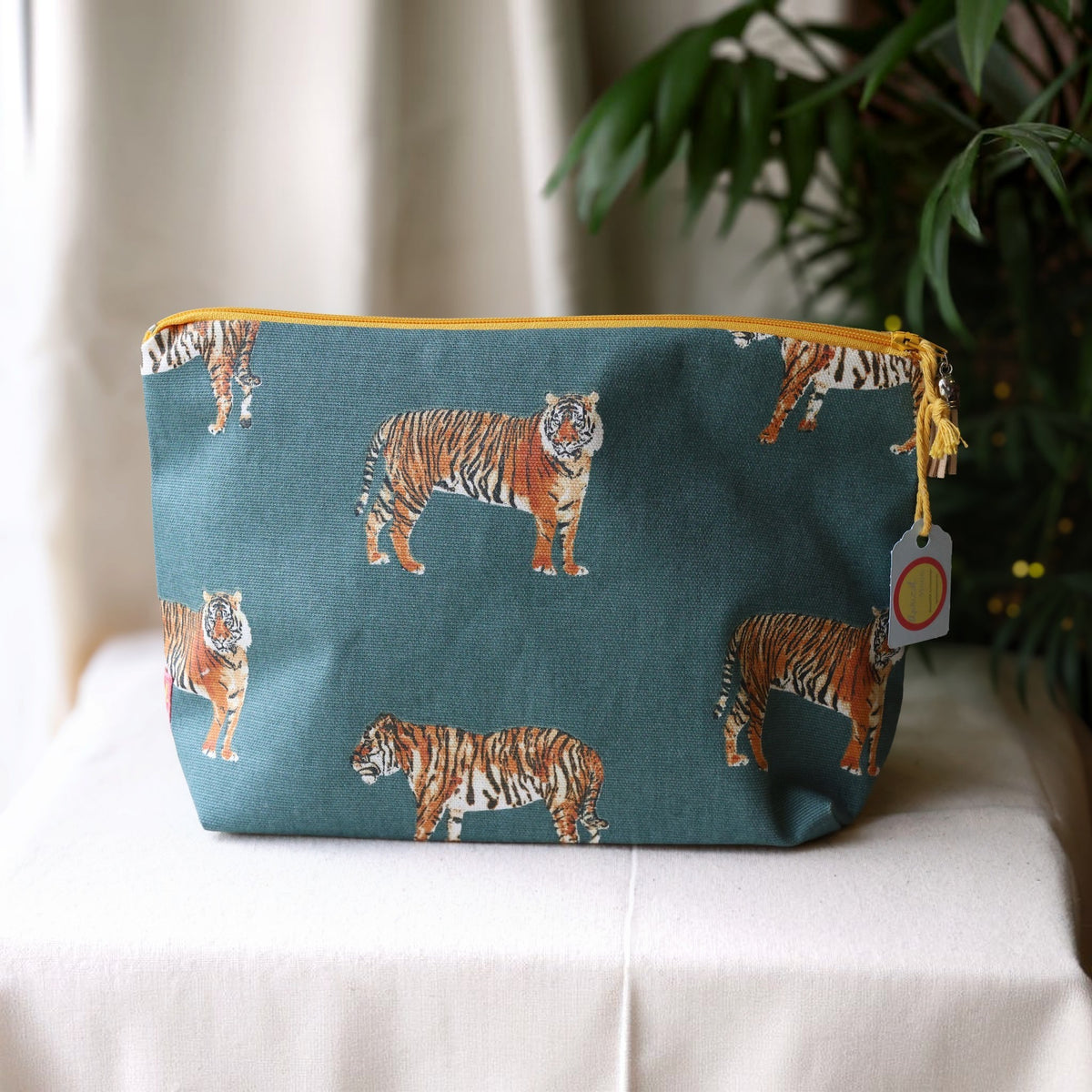 Tiger Tiger wash bag with a mustard yellow zip on a cream cloth beside a palm plant