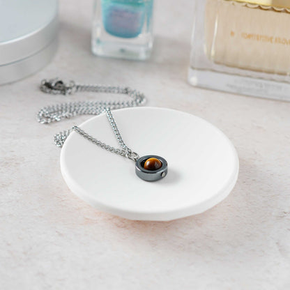 Necklace with a pendant on a white dish, with nail polish and perfume in the background