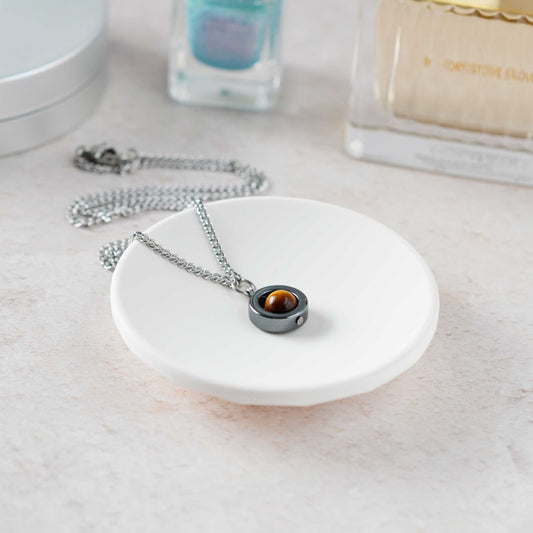Necklace with a pendant on a white dish, with nail polish and perfume in the background
