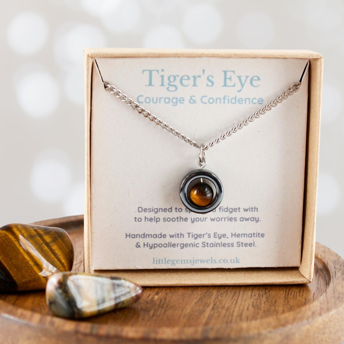 Tiger's Eye necklace with pendant on a display card, surrounded by stones on a wooden surface.