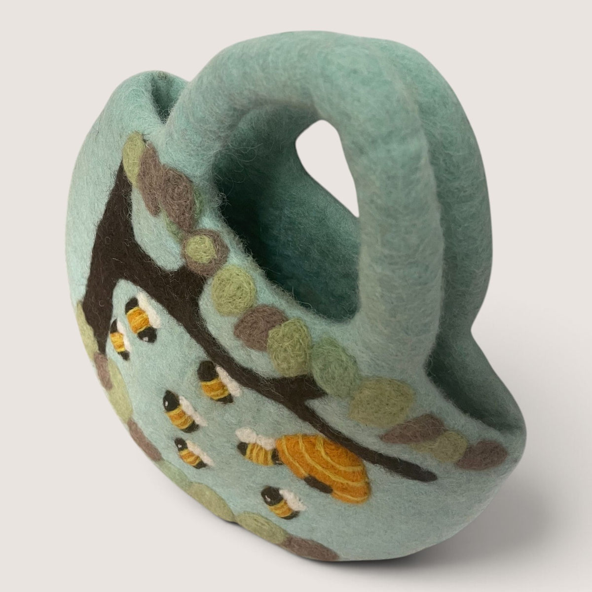 Side view of the Tree and Beehive Felted Bag showing the rounded shape, felted handle and bee design
