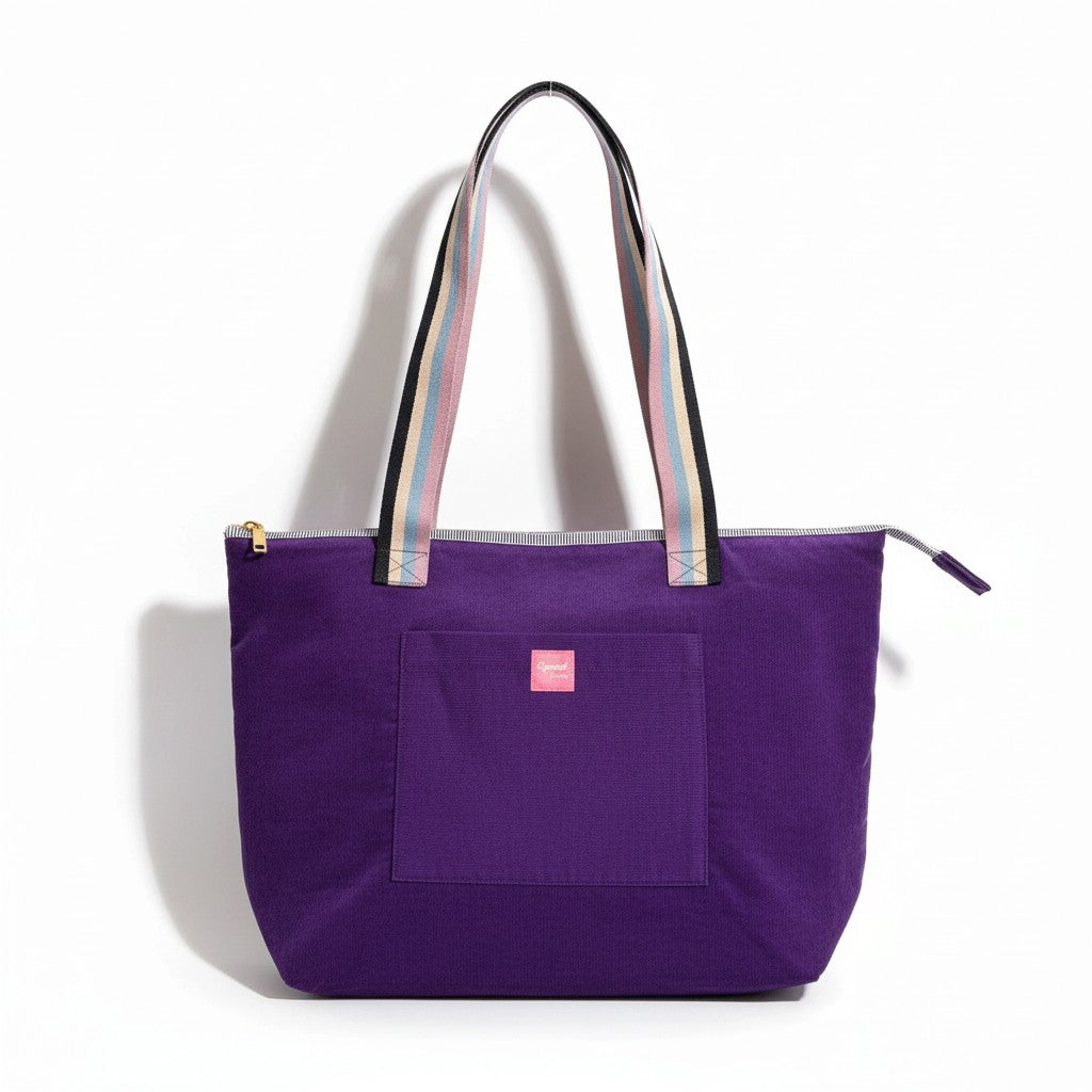 Twilight Bloom shoulder tote in purple corduroy with rainbow striped handles and a pink Apricot Moon label on the front pocket, front view on a white background, handmade in Dorset