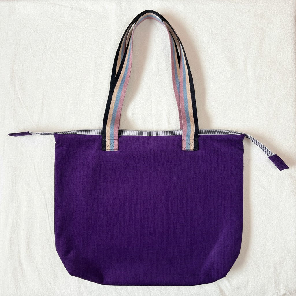 Rear view of the Twilight Bloom purple corduroy shoulder tote with striped handles and no pocket, laid flat on a cream cloth