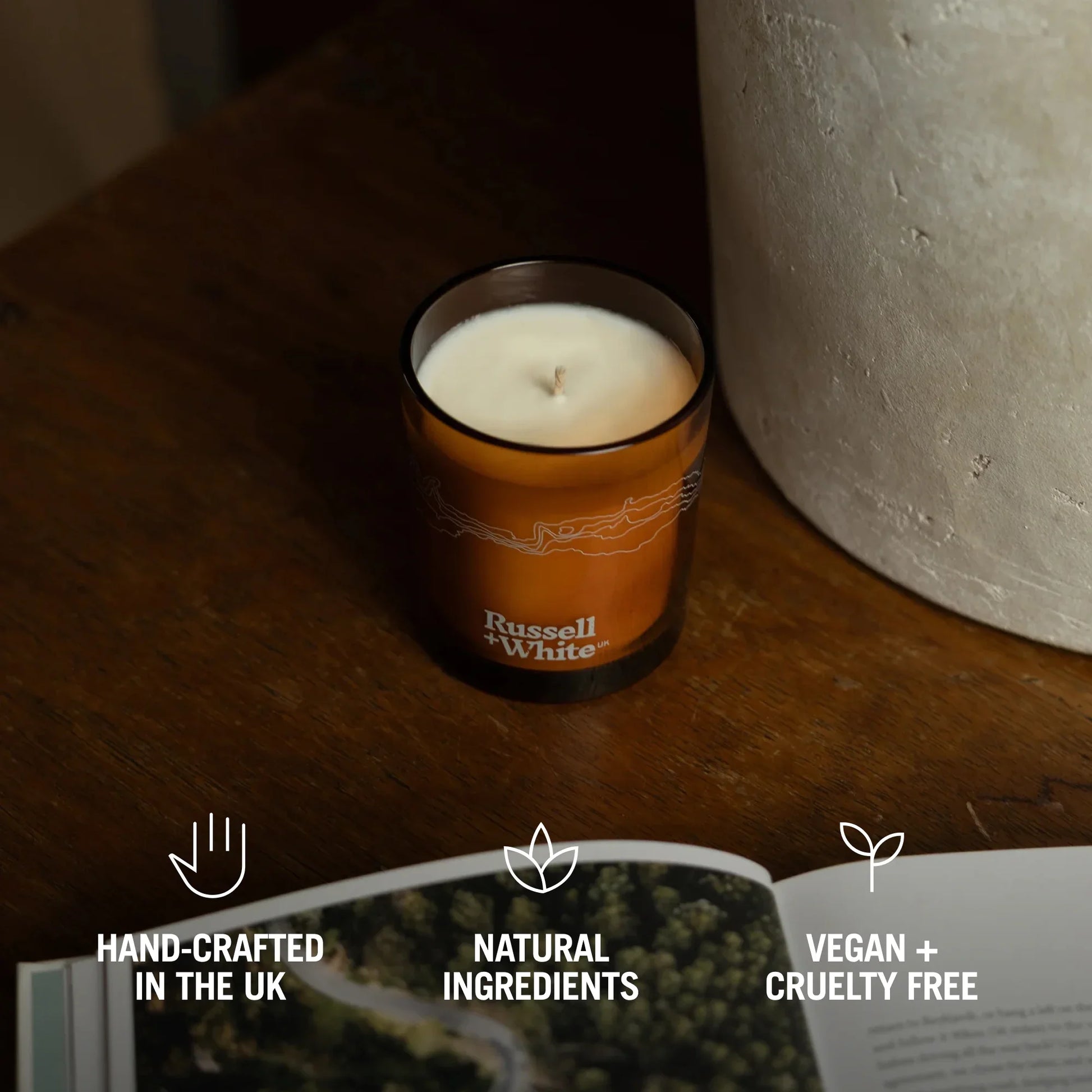 Candle in an orange container with 'Russell & White' branding on a wooden surface.