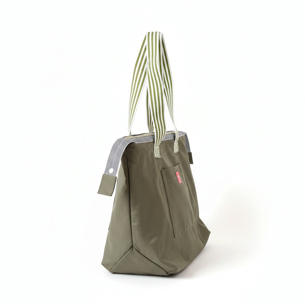 Side view of the Wild Sage shoulder tote showing the olive green body, striped handles, front pocket and pink label