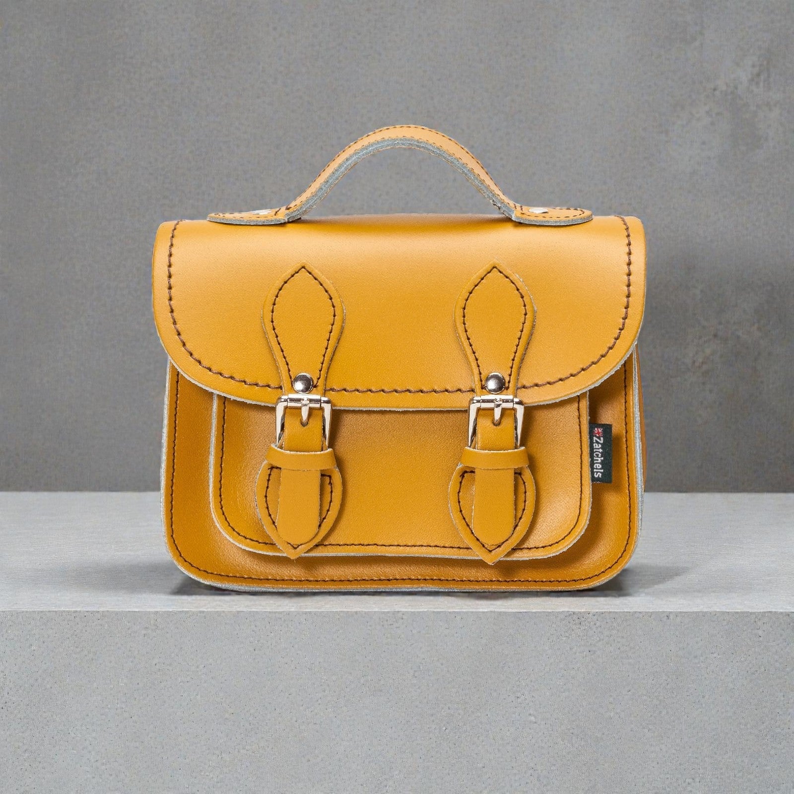 Yellow leather satchel bag with metal buckles on a gray background