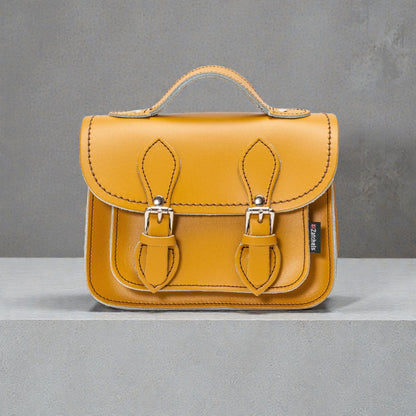 Yellow leather satchel bag with metal buckles on a gray background