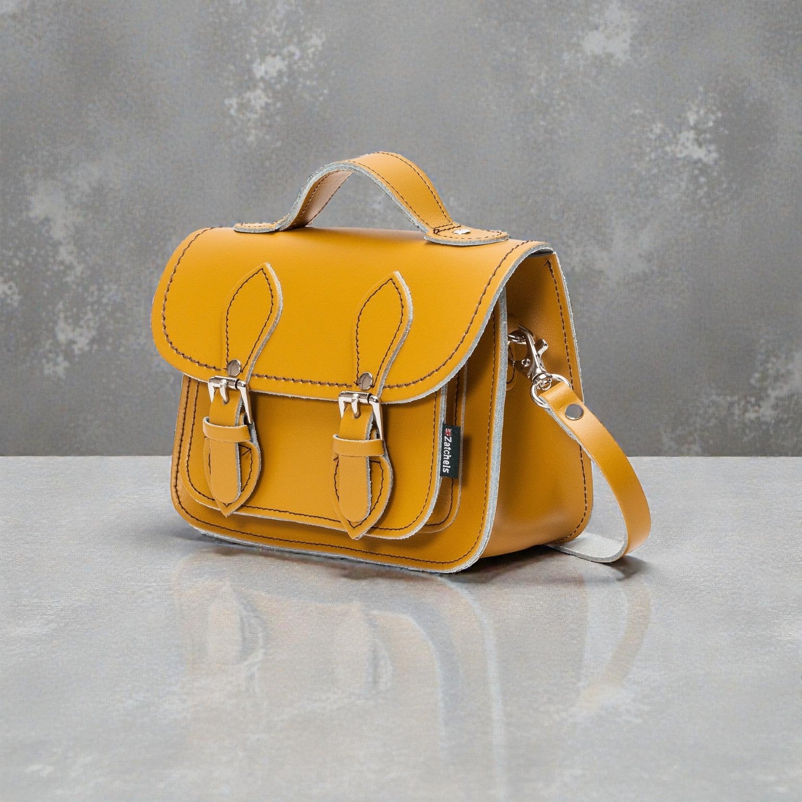 Yellow leather satchel bag on a gray surface with a gray background