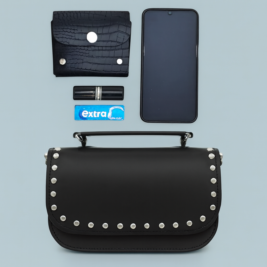 Black studded handbag with phone, wallet, and other items on a light blue background