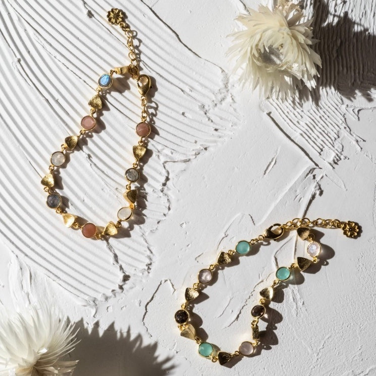 Gold necklace with multicolored stones on a textured white surface with flowers.