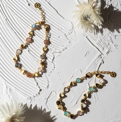 Gold necklace with multicolored stones on a textured white surface with flowers.
