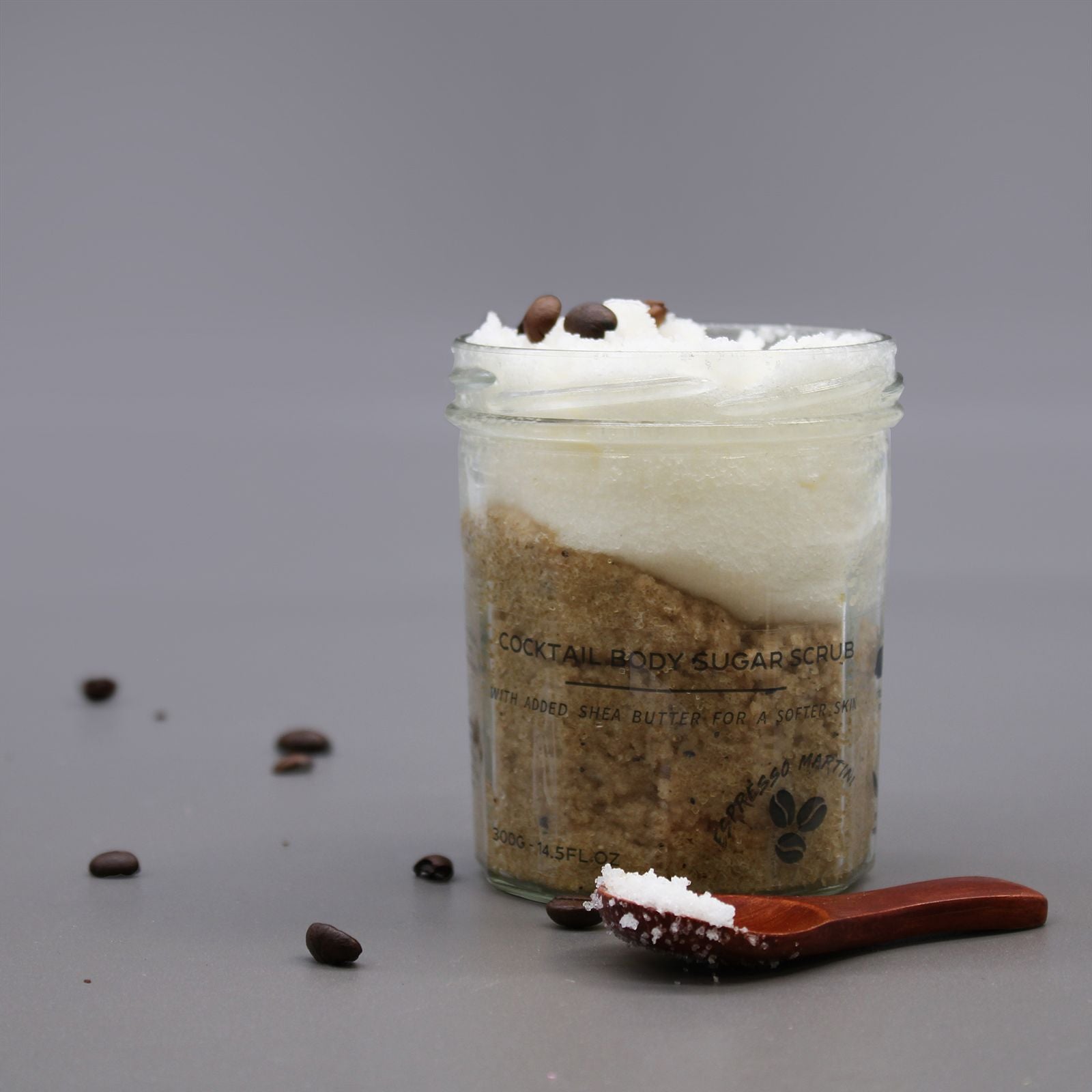 Jar of cocktail body sugar scrub with a wooden scoop on a gray background