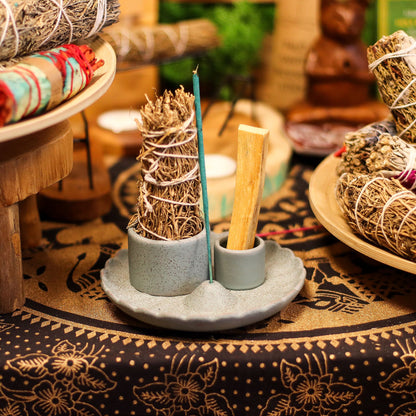 Incense sticks and cones on a ceramic holder with a patterned tablecloth in the background