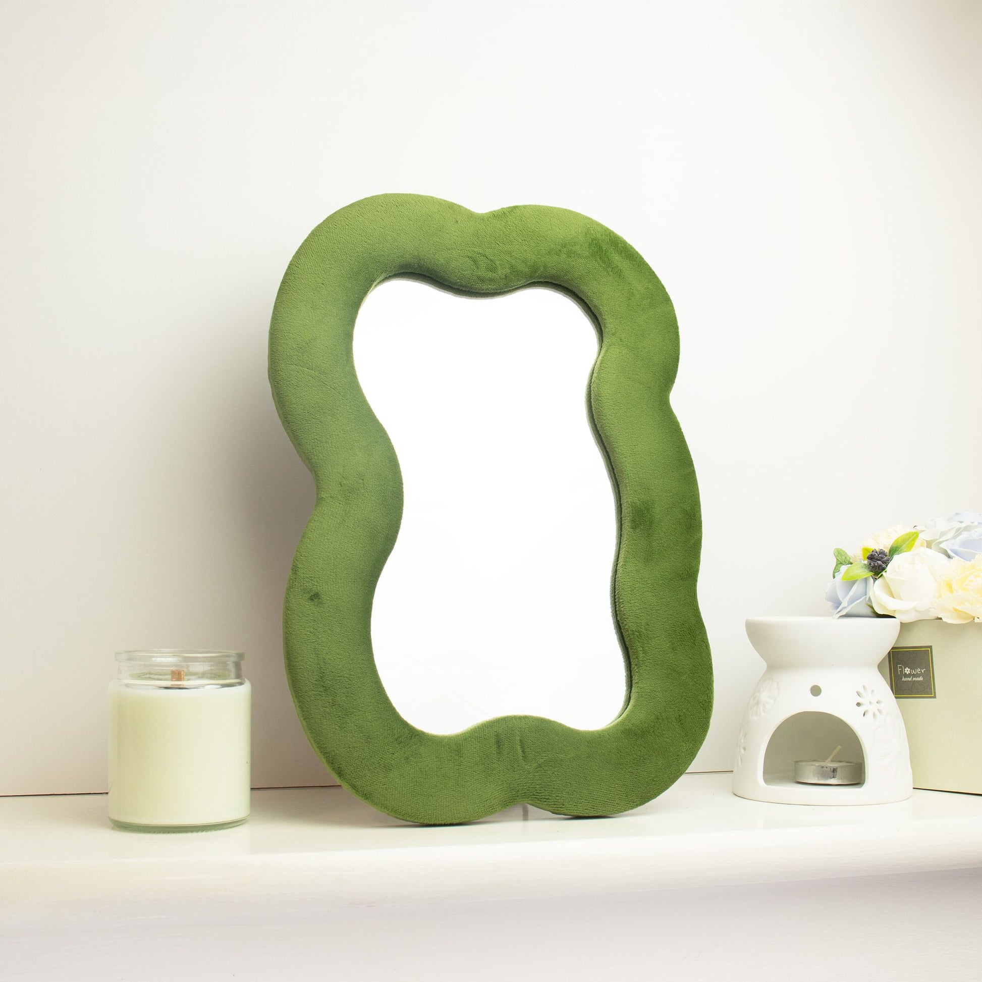 Green textured mirror on a white surface with a candle and decorative items in the background.