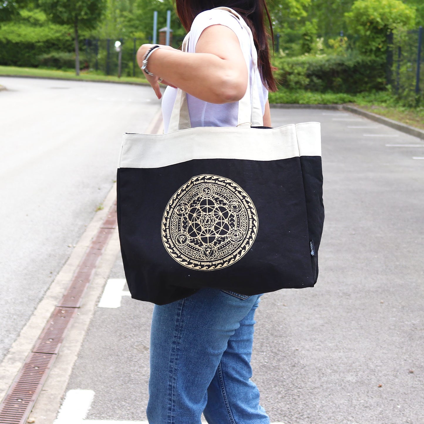 Person holding a black tote bag with a gold emblem on a street.