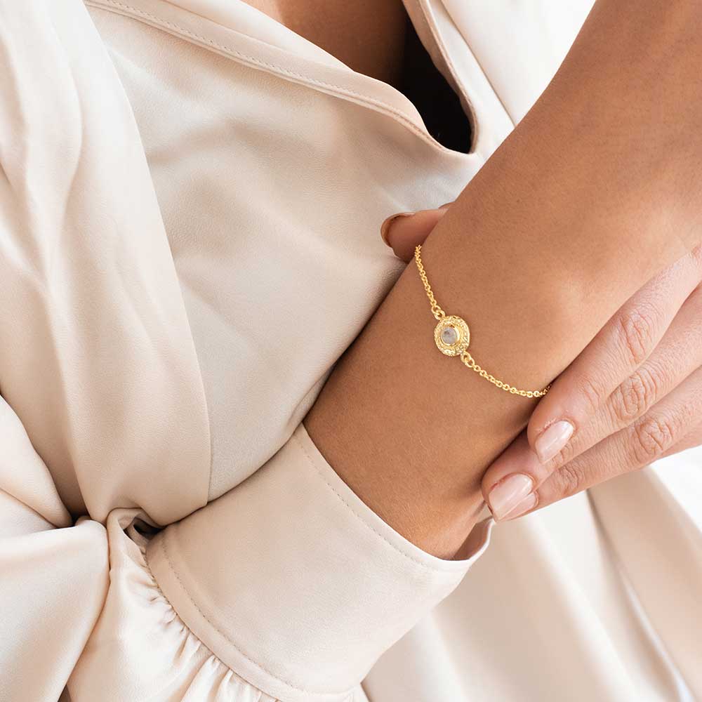 Gold bracelet on a wrist with a neutral background