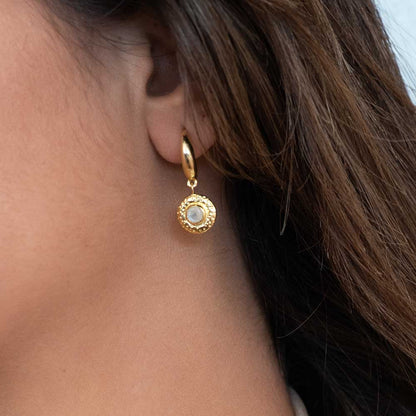 Close-up of a person wearing a gold earring with a gemstone.