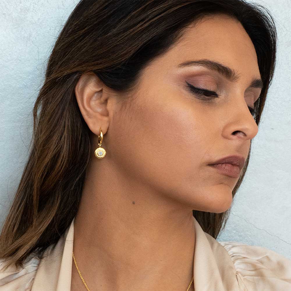 Close-up of a woman wearing gold earrings and a necklace against a light background
