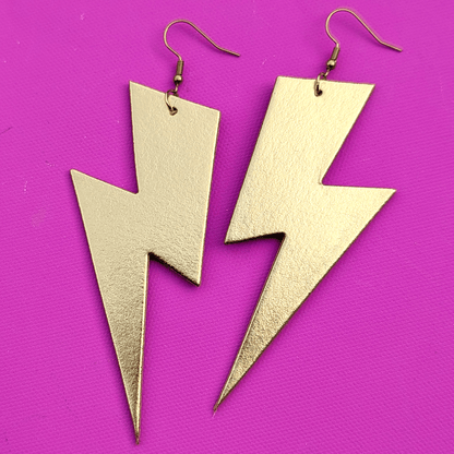 Gold lightning bolt earrings on a purple background