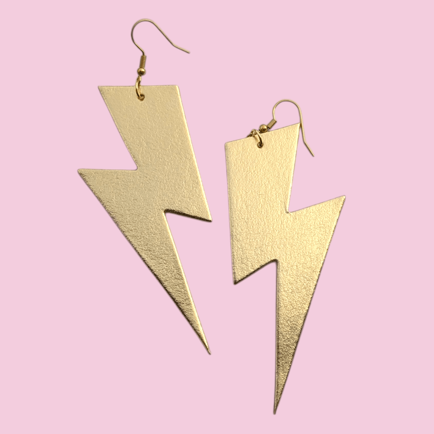 Gold lightning bolt earrings on a pink background