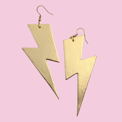 Gold lightning bolt earrings on a pink background