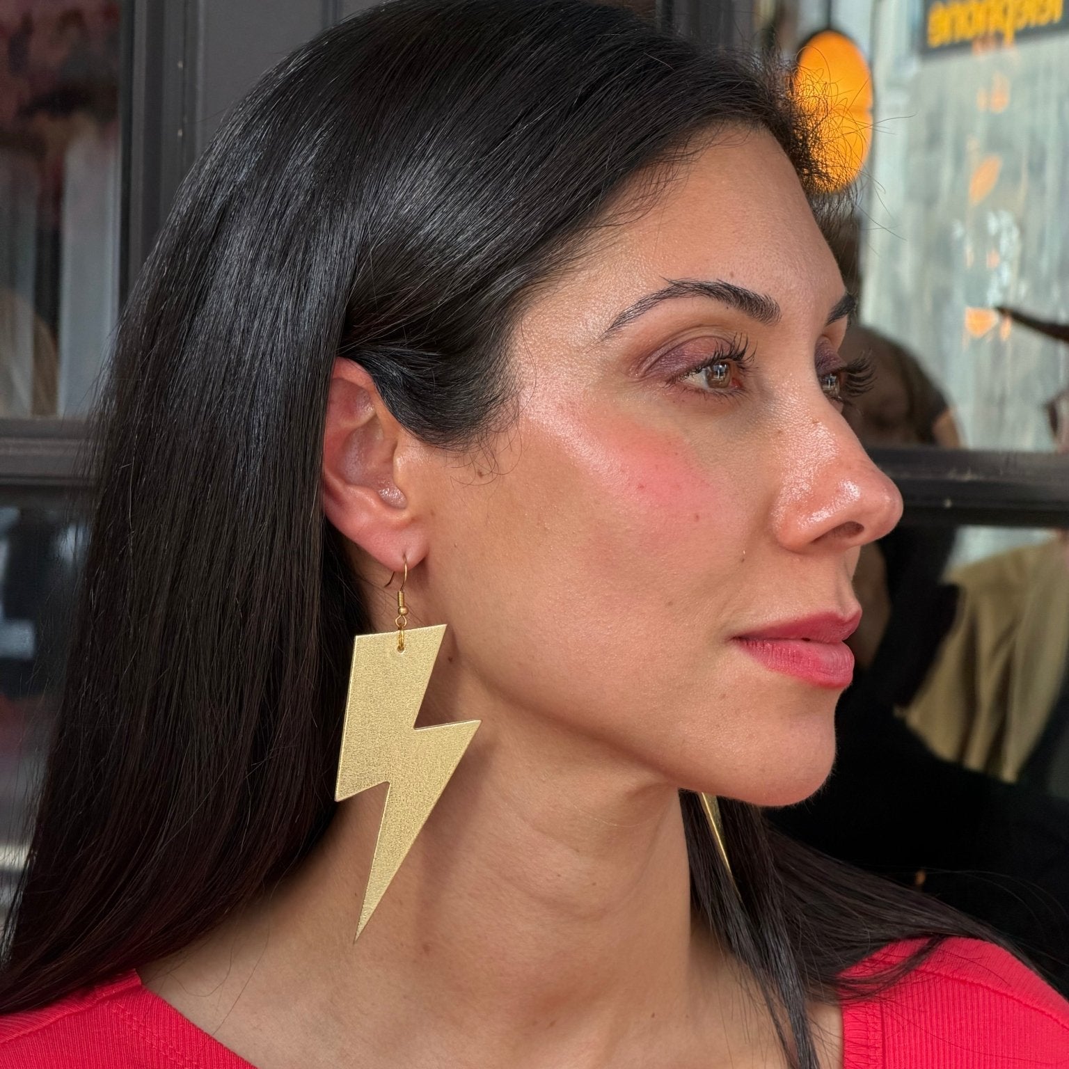 Woman wearing gold lightning bolt earrings with a blurred background