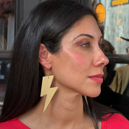 Woman wearing gold lightning bolt earrings with a blurred background