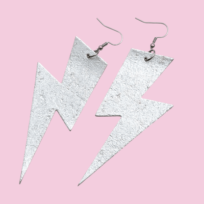 Silver lightning bolt earrings on a pink background