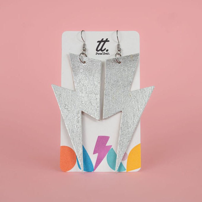 Pair of silver lightning bolt earrings on a colorful card against a pink background