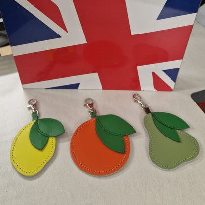 Three fruit-shaped keychains (lemon, orange, pear) in front of a Union Jack flag.