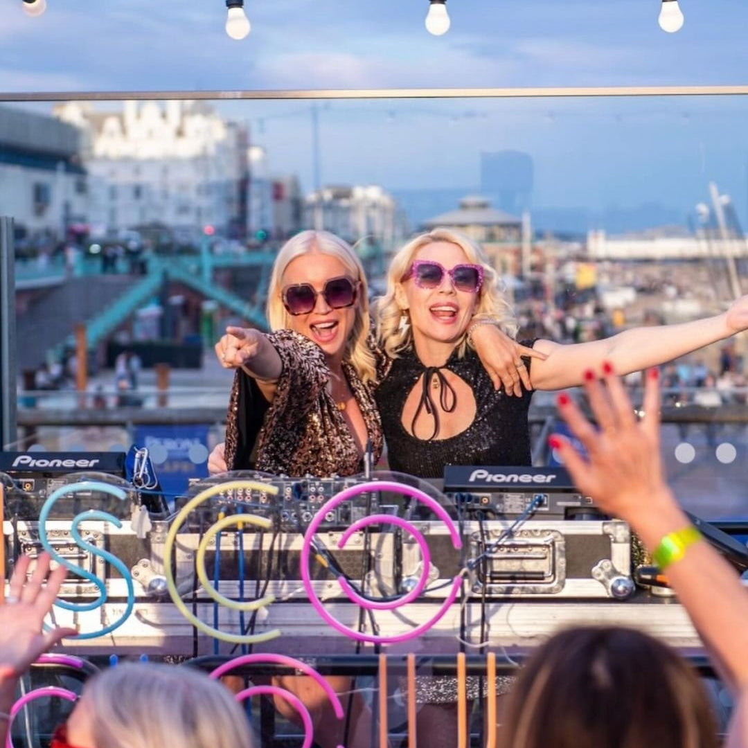 Two DJs at a rooftop party with cityscape in the background