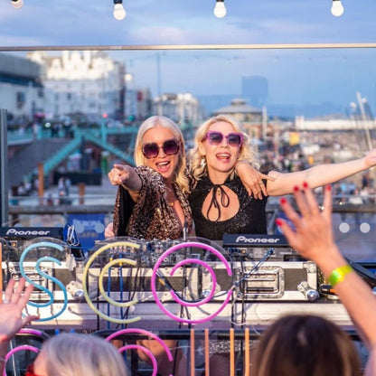 Two DJs at a rooftop party with cityscape in the background