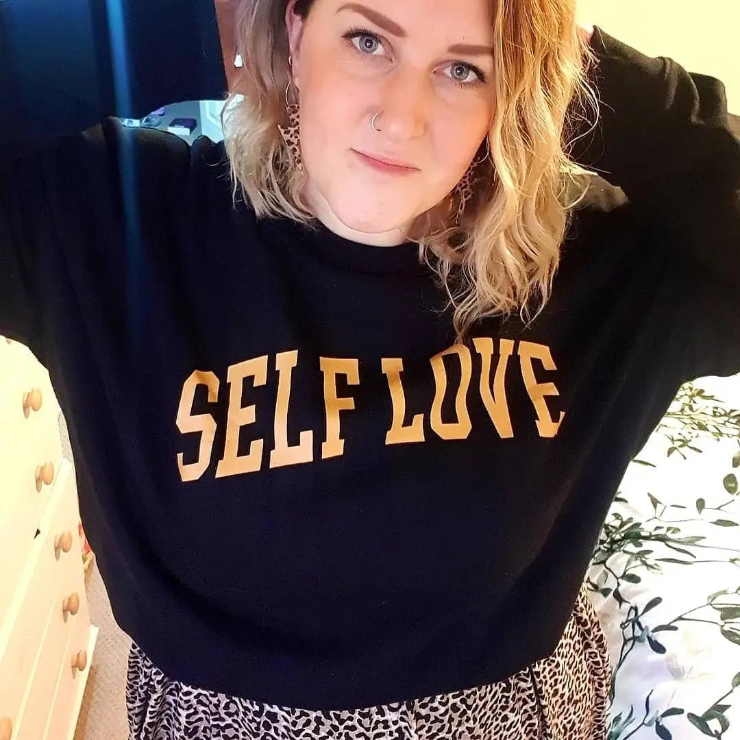 Person wearing a black sweatshirt with 'SELF LOVE' text in a casual setting