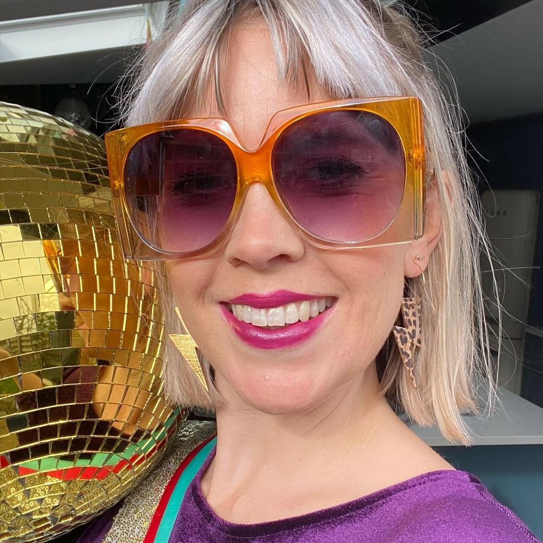 Person wearing large orange sunglasses with a gold disco ball in the background