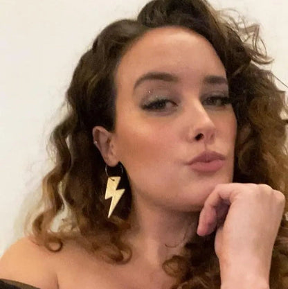 Woman wearing a gold lightning bolt earring with a plain background