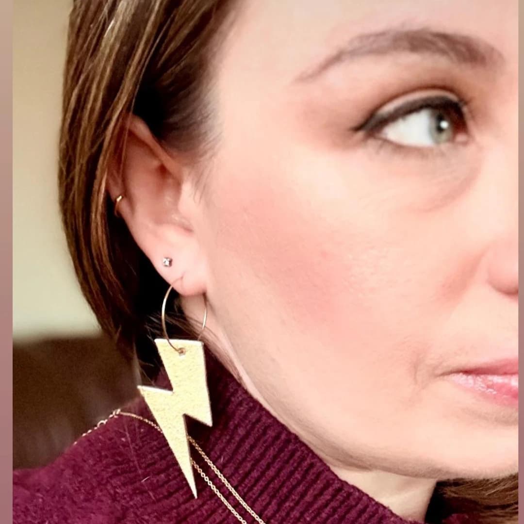 Close-up of a woman wearing gold lightning bolt earrings.